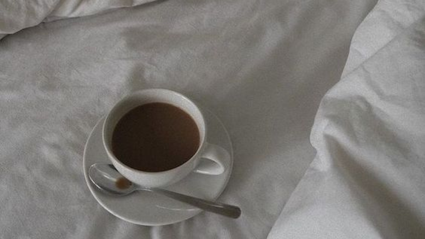 Strong, black cup of coffee on a white bedspread.