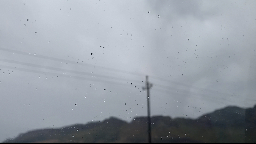 Through a rain splattered window, a heavy grey sky is threatening to split open and release rain.