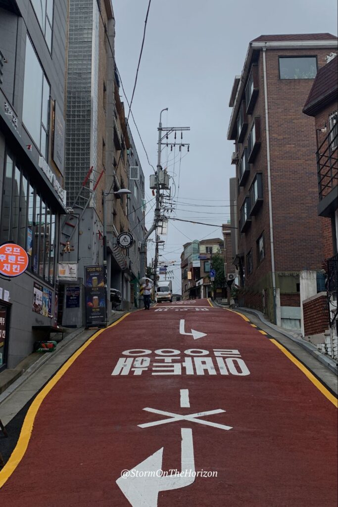 Street in Seoul, South Korea. This red street is in Itaewon, Seoul. It's lined with red-bricked buildings and has white directional signs on the groun. Shared in Storm on the Horizon's ultimate travel guide to South Korea.