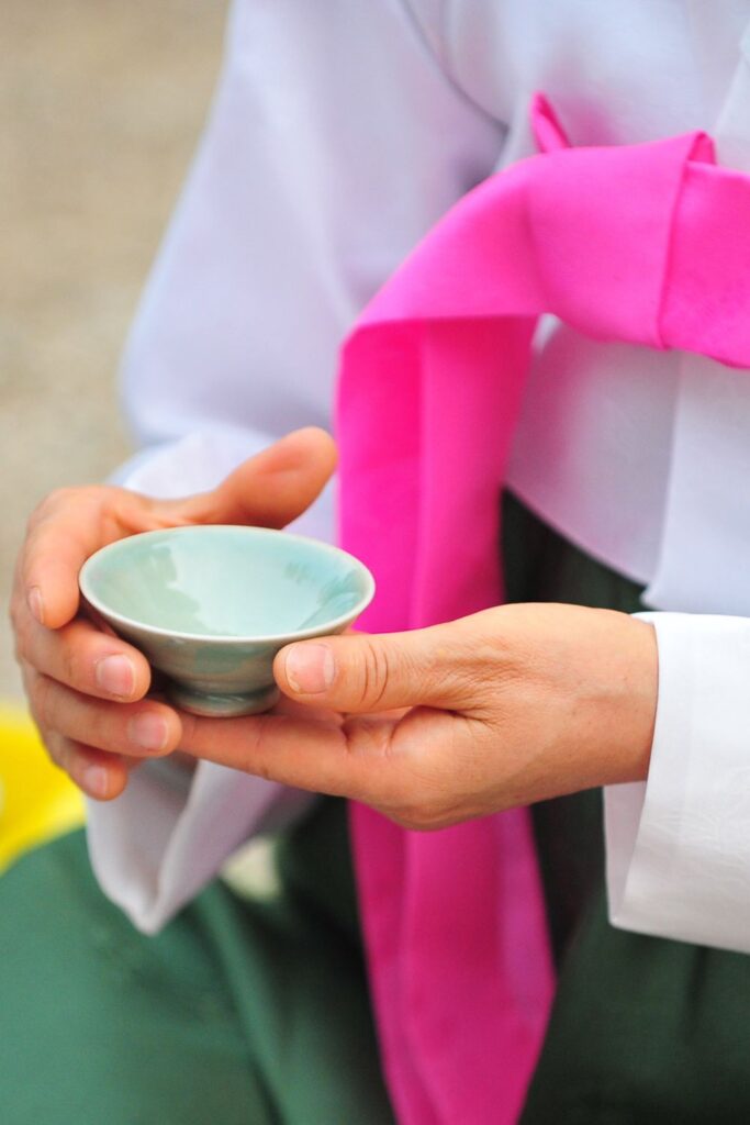 Woman in Korea wearing hanbok. She is holding a Korean teacup and taking part in a traditional tea ceremony. Storm on the Horizon shares must-do workshops when you're travelling in South Korea.