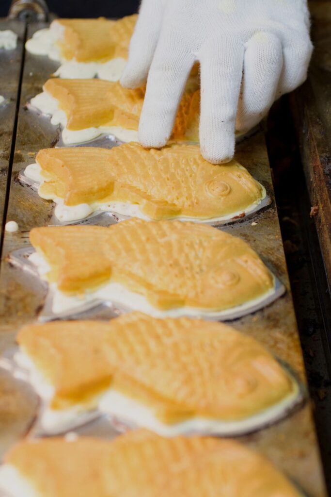 Scenes from Myeongdong street food market in Seoul where a gloved hand is making carp bread. The pastries - resembling fish - are lined up in a waffle iron and being flipped by the worker.