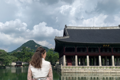 A girl stands in Seoul, South Korea. She is looking at Gyeongbok Palace so you can't see her face. She is wearing Hanbok - a traditional Korean outfit - in a light pink shade. She is a traveller, solo travelling in Seoul. Shared on Storm on the Horizon: A travel site for female travellers in the UK, Europe and South Korea.