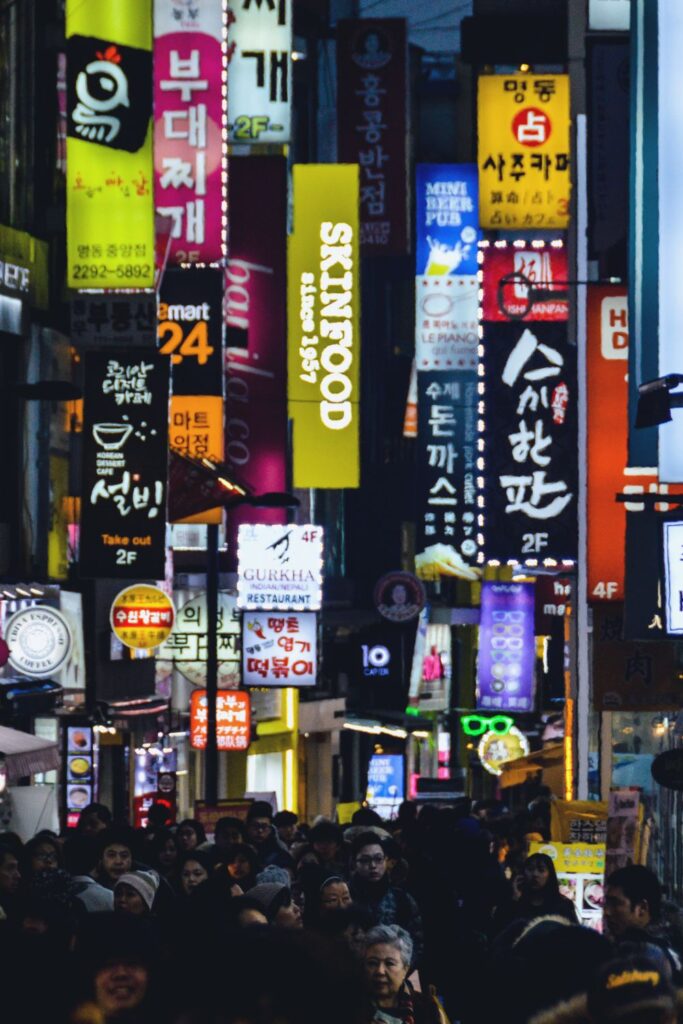 Scenes from Myeongdong Night Market at night: There are an overwhelming amount of billboards all illuminated and a bustling street of people below them, walking through Seoul. Shared on Storm on the Horizon: A travel site for solo travellers.